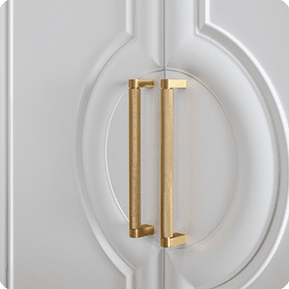 Close-up of an elegant cabinet door featuring a white, intricately molded design with a pair of sleek, gold rectangular handles. The hardware adds a touch of luxury and sophistication to the classic decorative paneling, making it a standout element in any interior design.